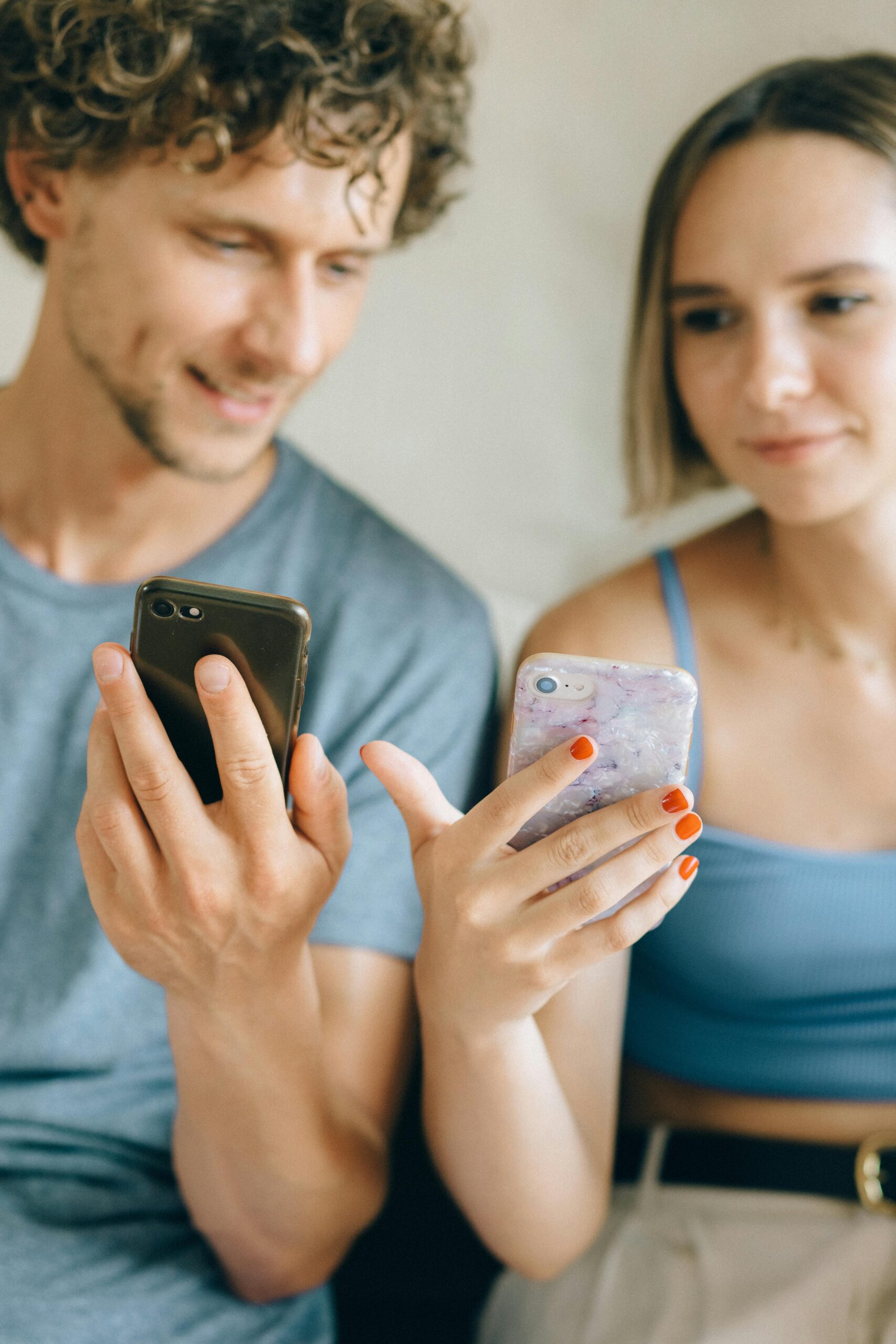 A close-up of a young couple sitting indoors, using smartphones together.
